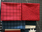 Four folded fabric pieces are stacked: two red fabrics on top, one plaid and one with a small floral pattern, and two blue fabrics below, one plaid and one with text.
