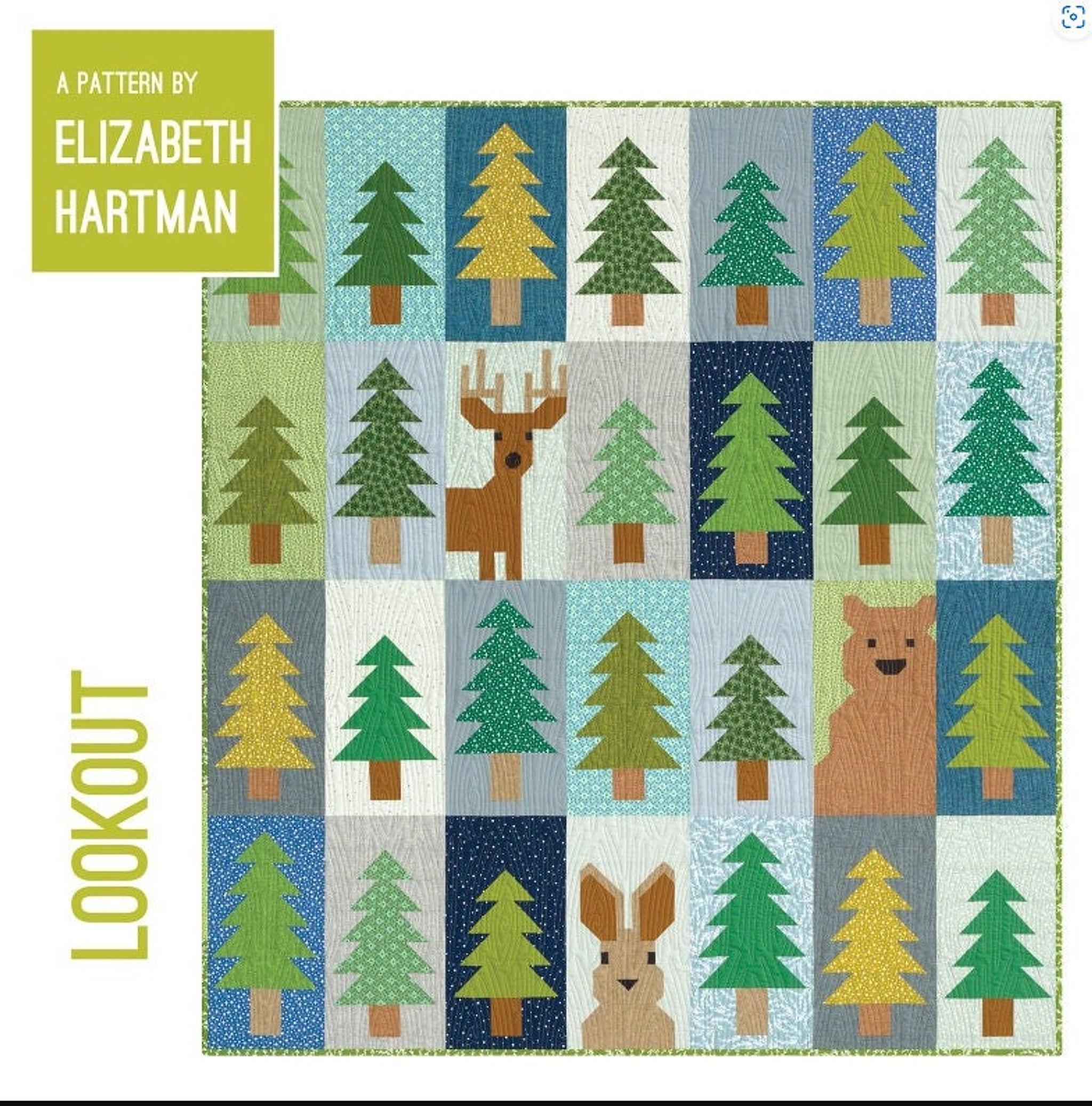 A quilt with a grid pattern of green trees, a brown deer, a brown bear, and a brown rabbit on light blue, dark blue, and tan squares, with "A PATTERN BY ELIZABETH HARTMAN" and "LOOKOUT" text.