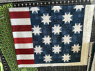 A quilt top with red and white stripes on the left and blue fabric with white stars on the right, lying on a green cutting mat.